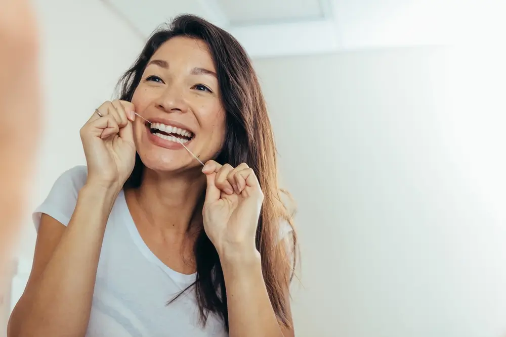 Woman looking in the bathroom mirror and using dental floss to clean her teeth