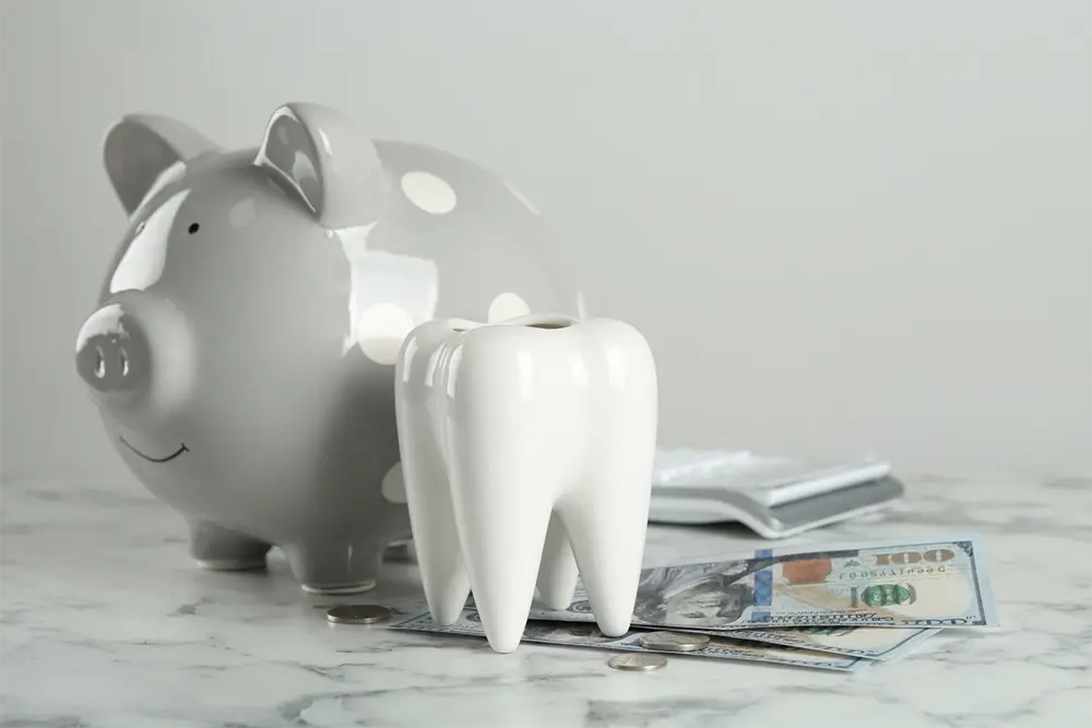 Ceramic model of tooth, piggy bank and money on white marble table